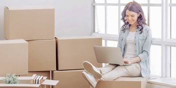 woman with laptop smiles sitting on boxes