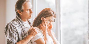 man standing behind upset woman hands on her shoulders