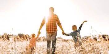 dad in field holding hands with two little kids