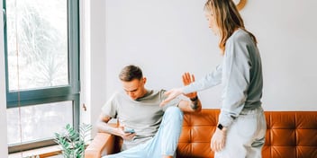 Young man on couch on cell phone ignoring female partner